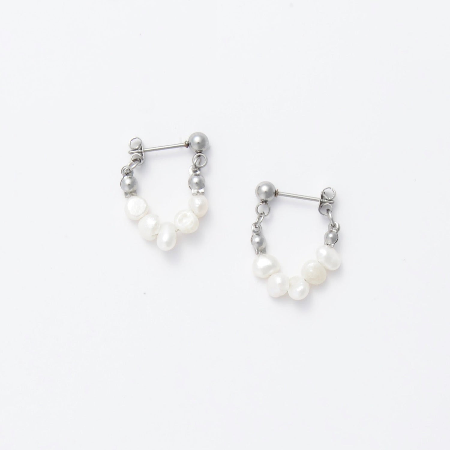 A pair of silver-colored thin pearl hoop earrings, displayed against a white background