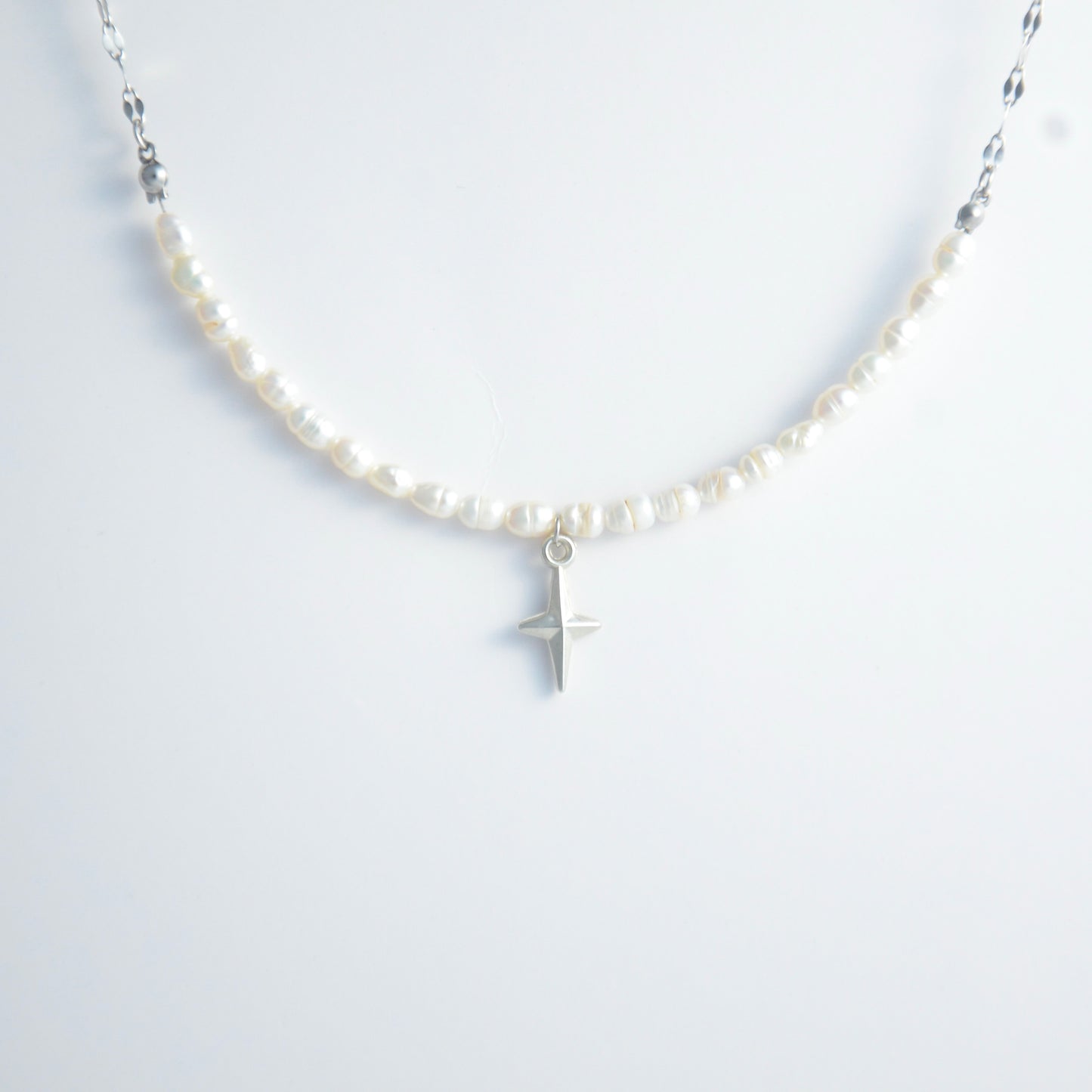 Silver pearl choker necklace with a small north star pendant on a light gray background