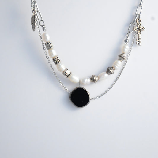 Silver charm necklace with black pendant and pearl-like beads on a white background