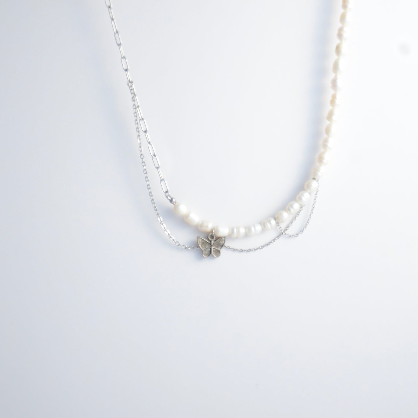 Silver necklace non-tarnish with pearl strands, layered chains and a silver butterfly pendant on a light gray background