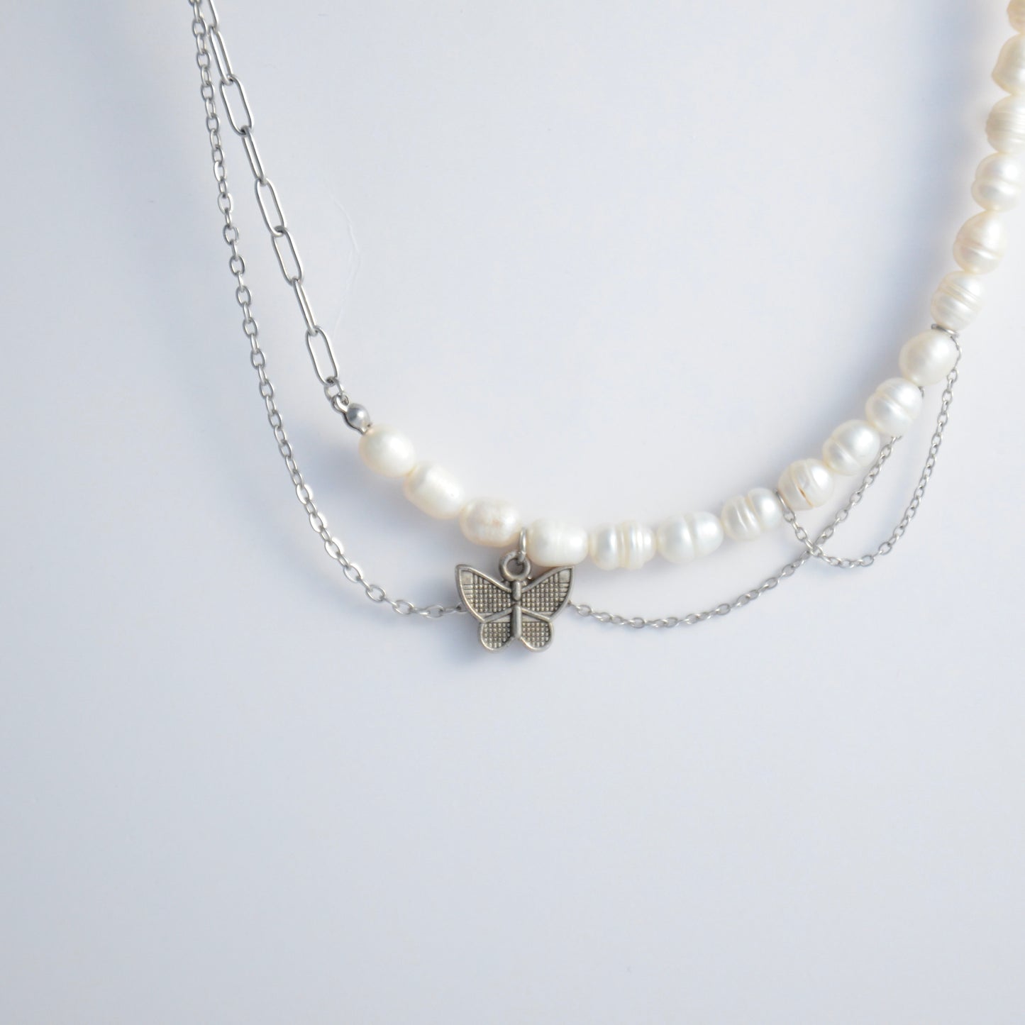 Silver necklace non-tarnish with pearl strands, layered chains and a silver butterfly pendant on a light gray background