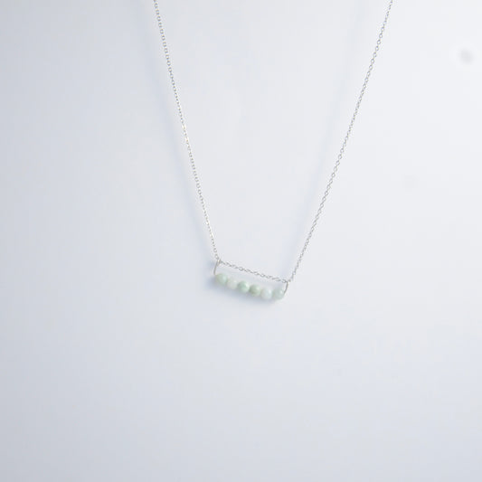 Silver necklace with a pendant made of jade beads on a light gray background