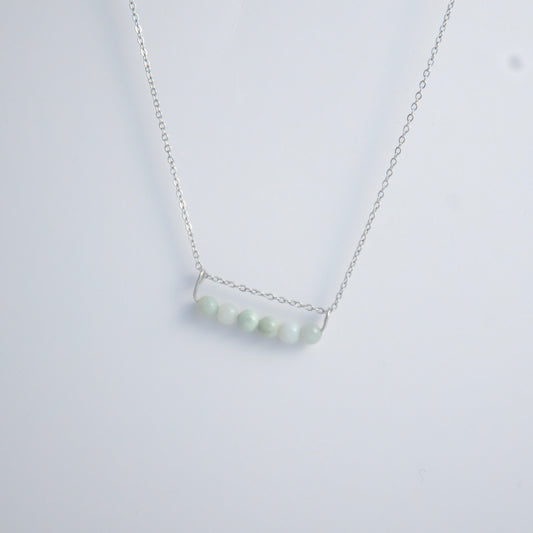 Silver necklace with a pendant made of jade beads on a light gray background