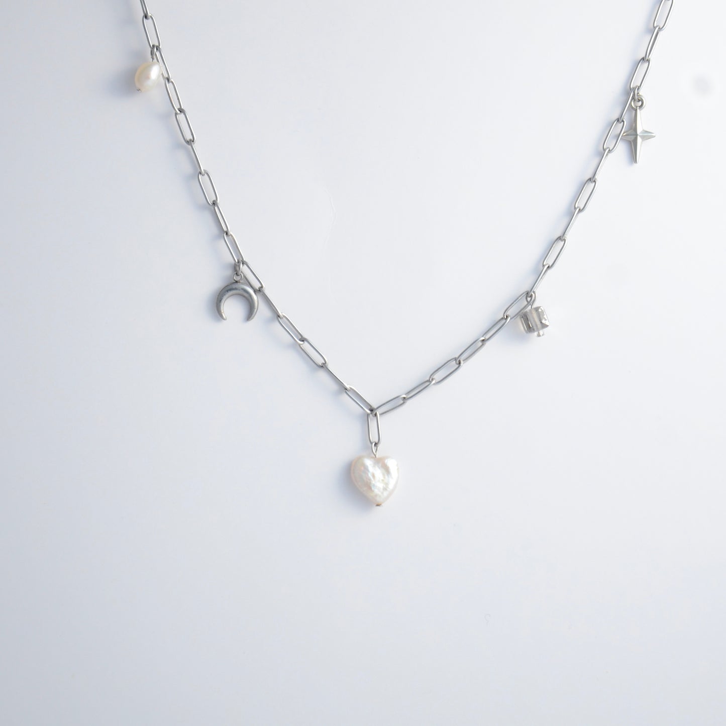 Silver chain charm necklace with pearl pendants, glass bead, and star pendants on a light gray background