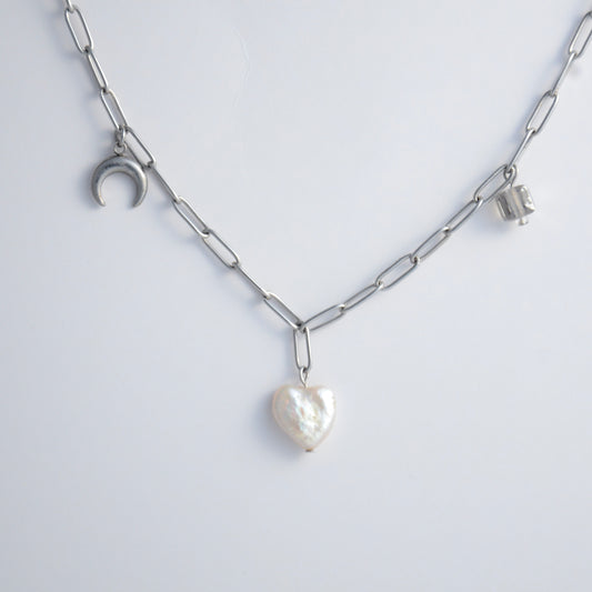 Silver chain charm necklace with pearl pendants, glass bead, and star pendants on a light gray background