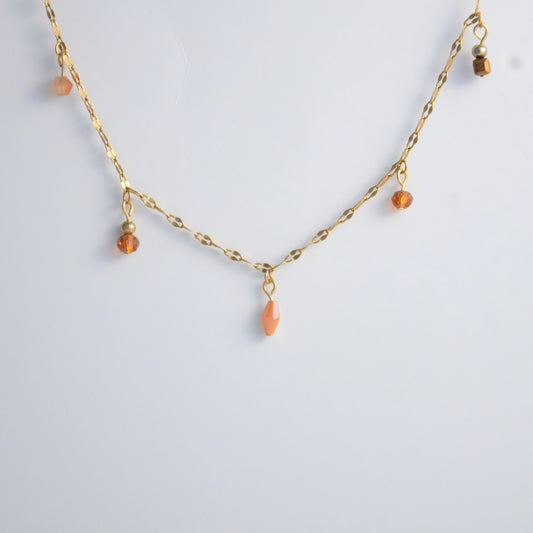 Delicate gold satellite necklace with small orange beads on a light gray background