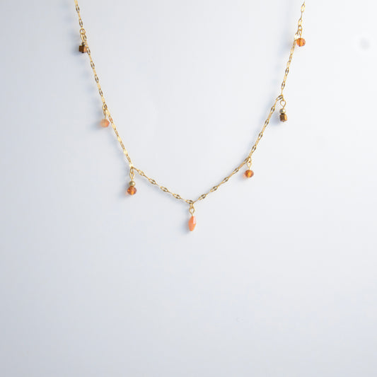 Delicate gold satellite necklace with small orange beads on a light gray background