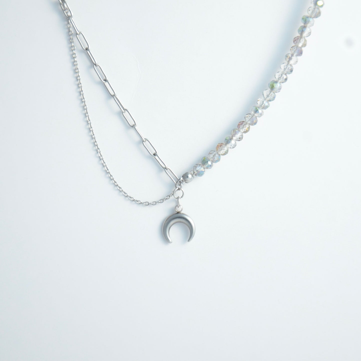 Silver layered necklace with a moon pendant and glass beads on a paperclip chain on a light gray background