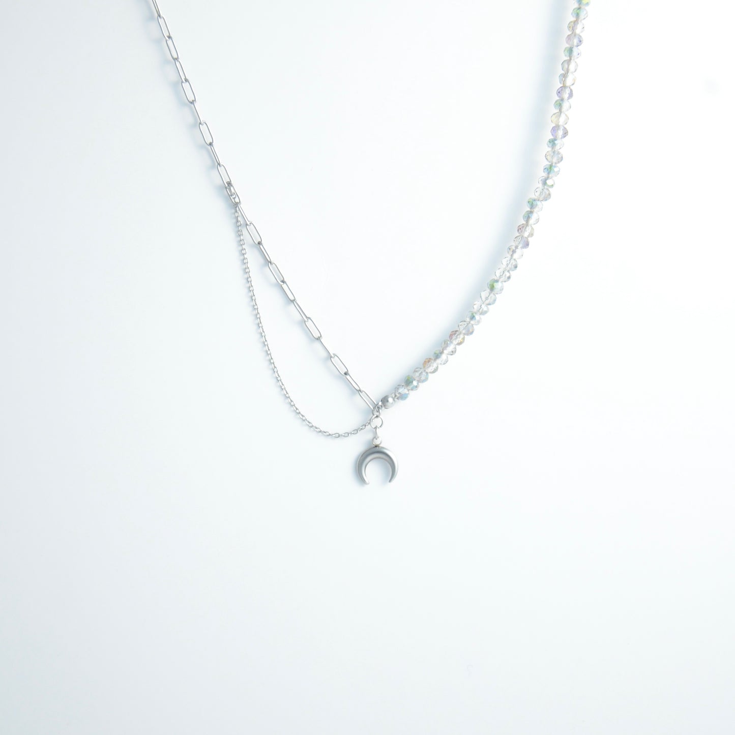 Silver layered necklace with a moon pendant and glass beads on a paperclip chain on a light gray background