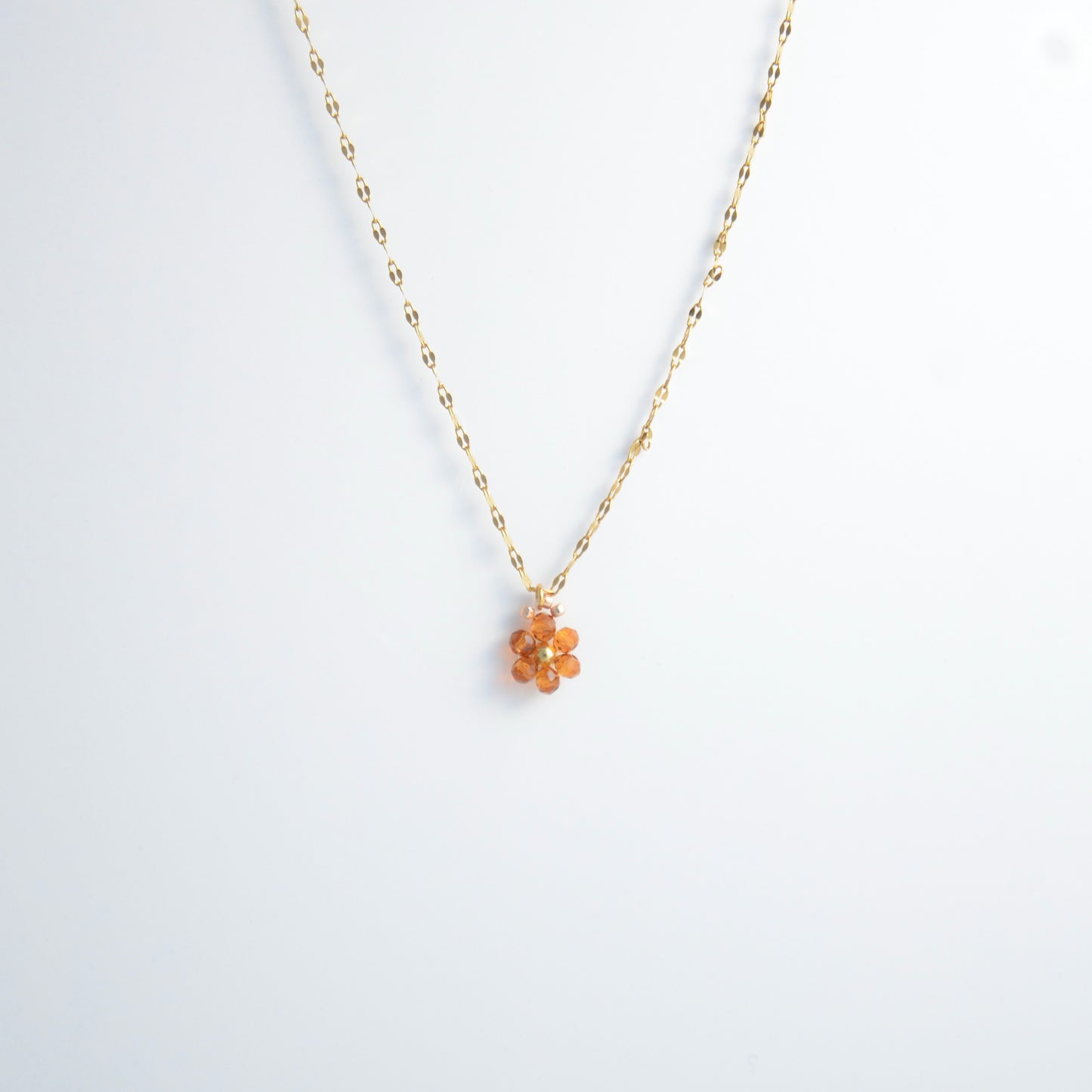 Gold necklace with a small orange flower pendant on a white background