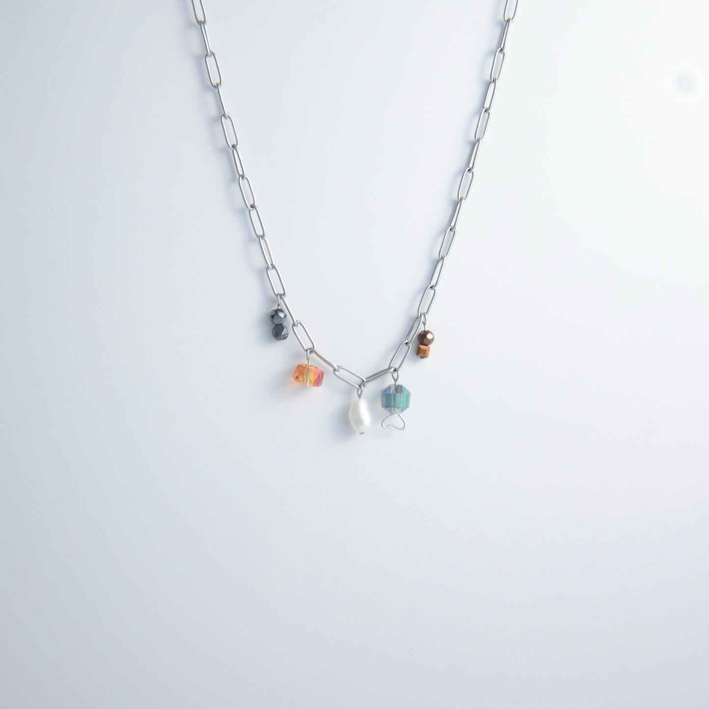 Silver paperclip chain necklace with small bead charms including freshwater pearls, black, blue, and orange glass beads on a light gray background