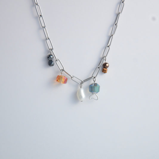 Silver paperclip chain necklace with small bead charms including freshwater pearls, black, blue, and orange glass beads on a light gray background