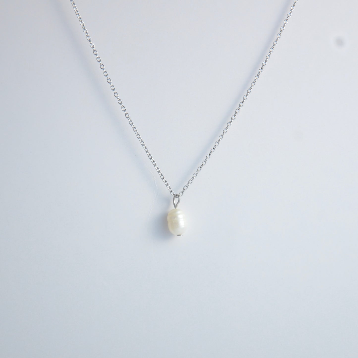 Silver dainty pearl necklace with freshwater pearl charm on a light gray background