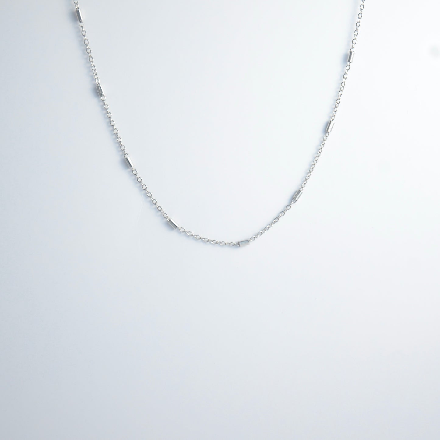 Dainty silver bar link chain for minimalistic fashion or for layering jewelry on a light gray background
