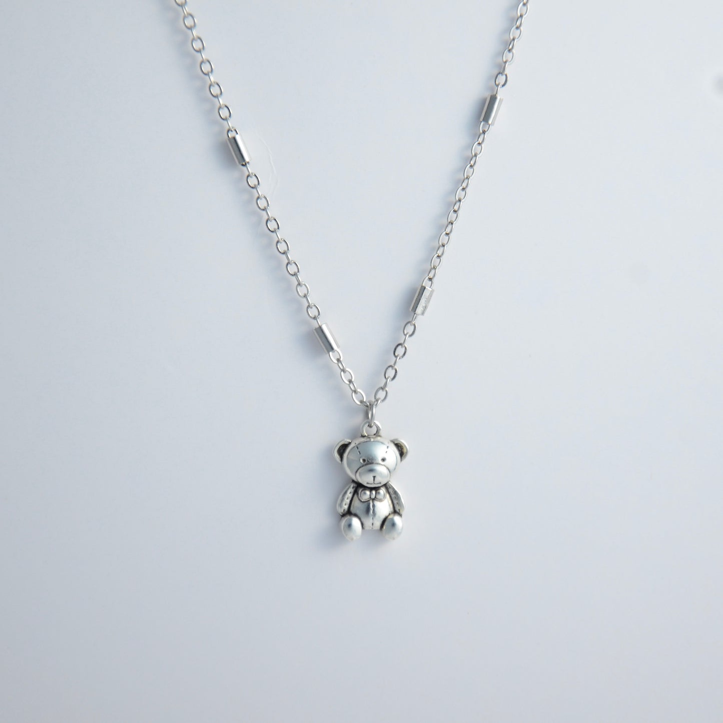 Dainty silver bar link chain with a teddy bear charm for minimalistic fashion or for layering jewelry on a light gray background
