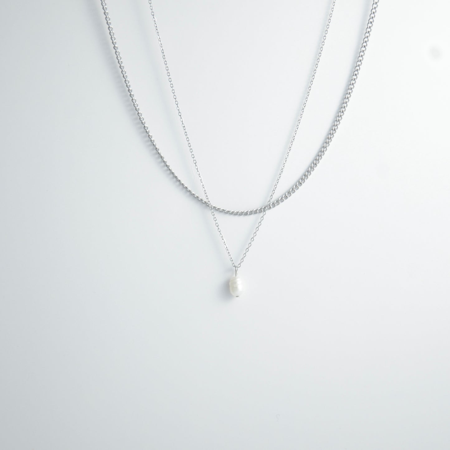 Silver stainless steel layered necklace set with a curb chain and a dainty pearl pendant necklace on a light gray background