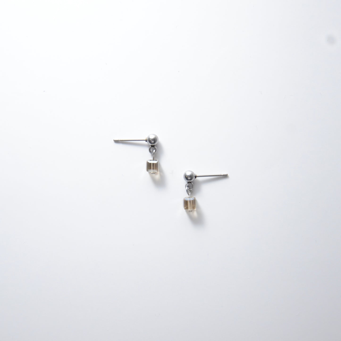Pair of silver stainless steel ball stud earrings with sugar cube gray glass beads on a white background