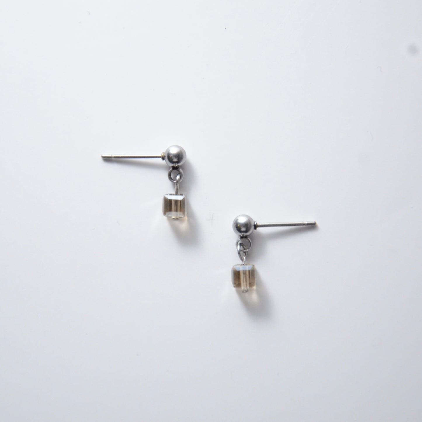 Pair of silver stainless steel ball stud earrings with sugar cube gray glass beads on a white background