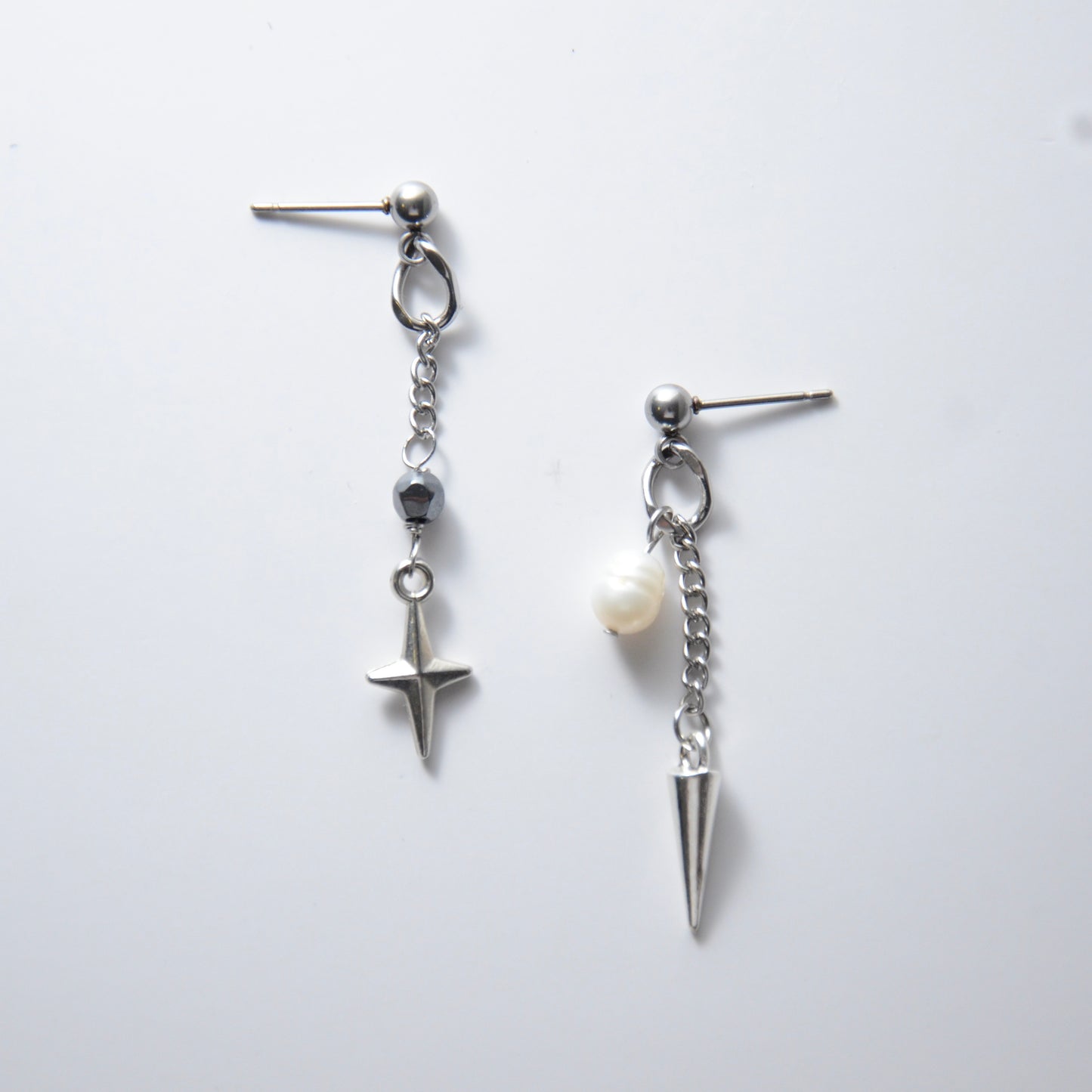 Pair of silver stainless steel ball stud drop earrings with a chain and star charm and a pearl and spike charm on a white background