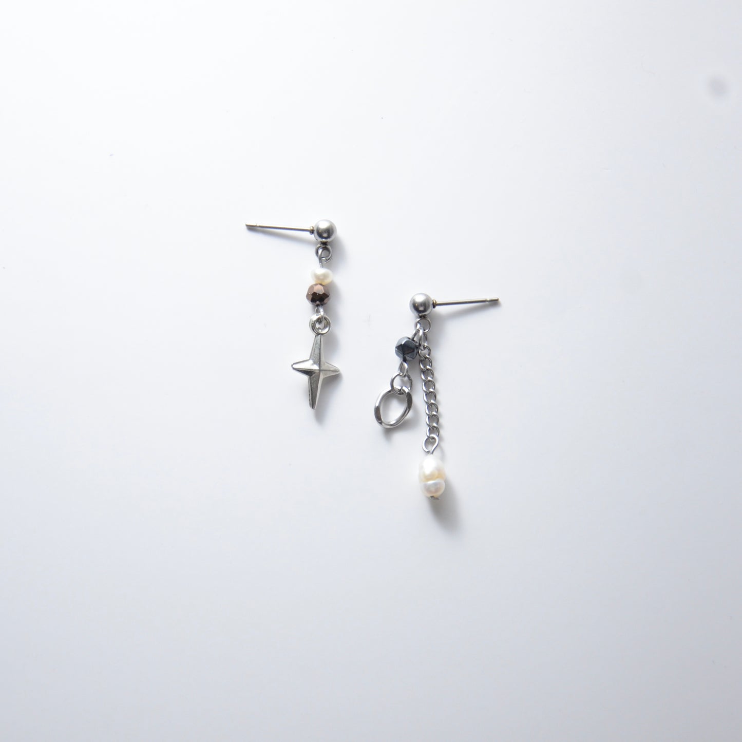 Pair of silver stainless steel ball stud drop earrings with orange and black glass beads and star and pearl charm with unique designs on a white background
