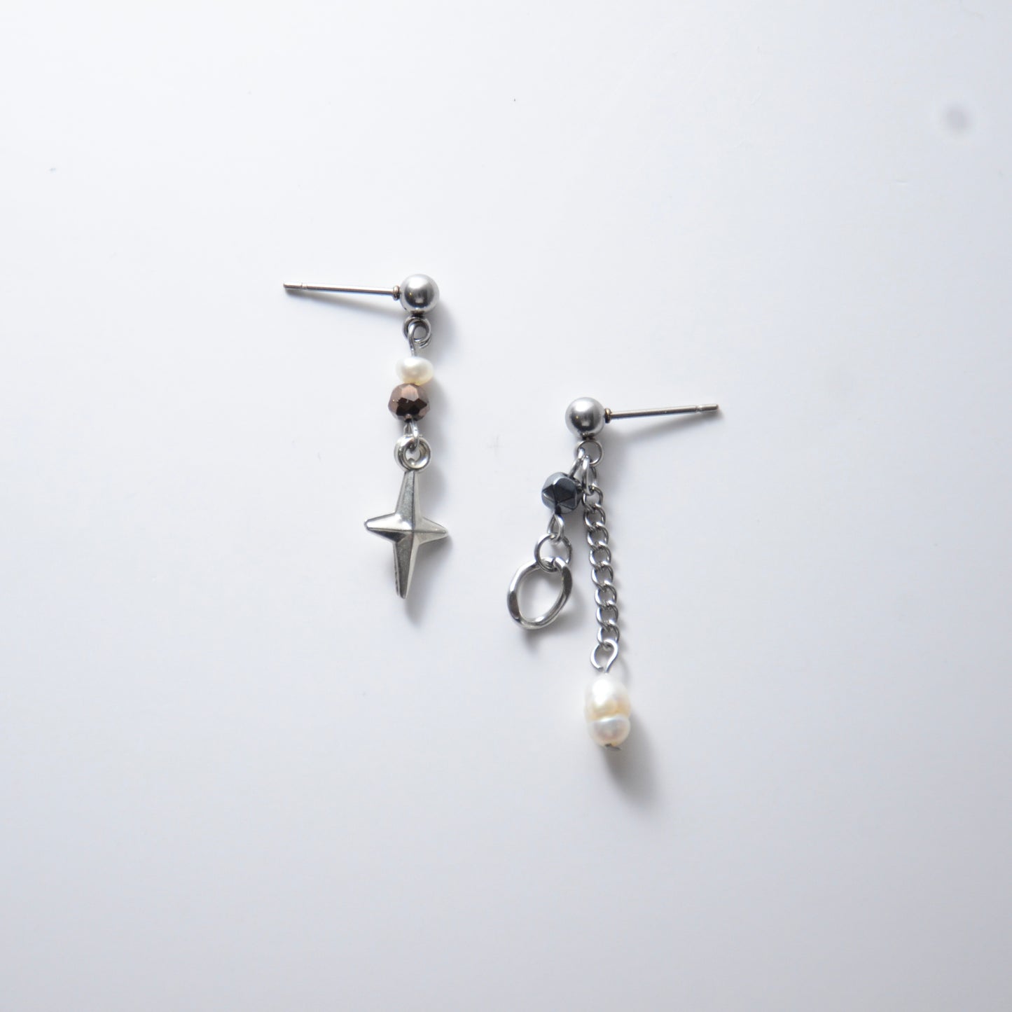 Pair of silver stainless steel ball stud drop earrings with orange and black glass beads and star and pearl charm with unique designs on a white background
