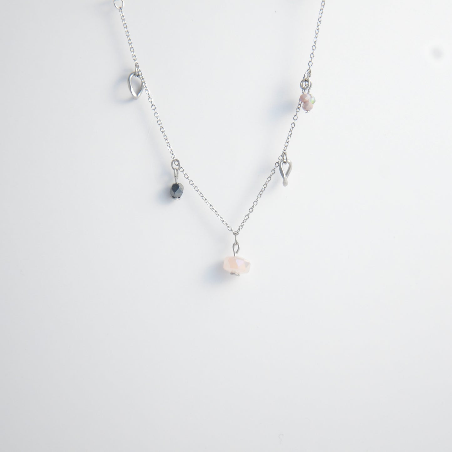 Silver stainless steel delicate charm necklace with small pink, black, purple glass beads and a geometric charm on a light gray background
