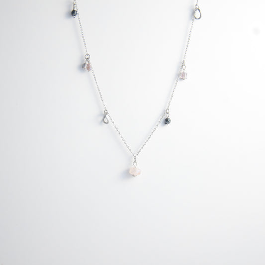 Silver stainless steel delicate charm necklace with small pink, black, purple glass beads and a geometric charm on a light gray background