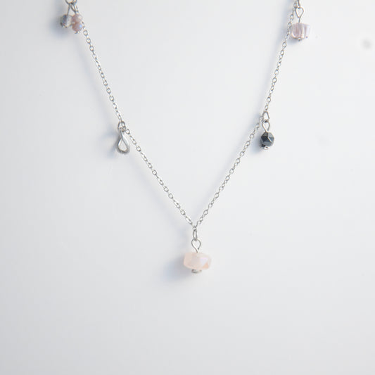 Silver stainless steel delicate charm necklace with small pink, black, purple glass beads and a geometric charm on a light gray background