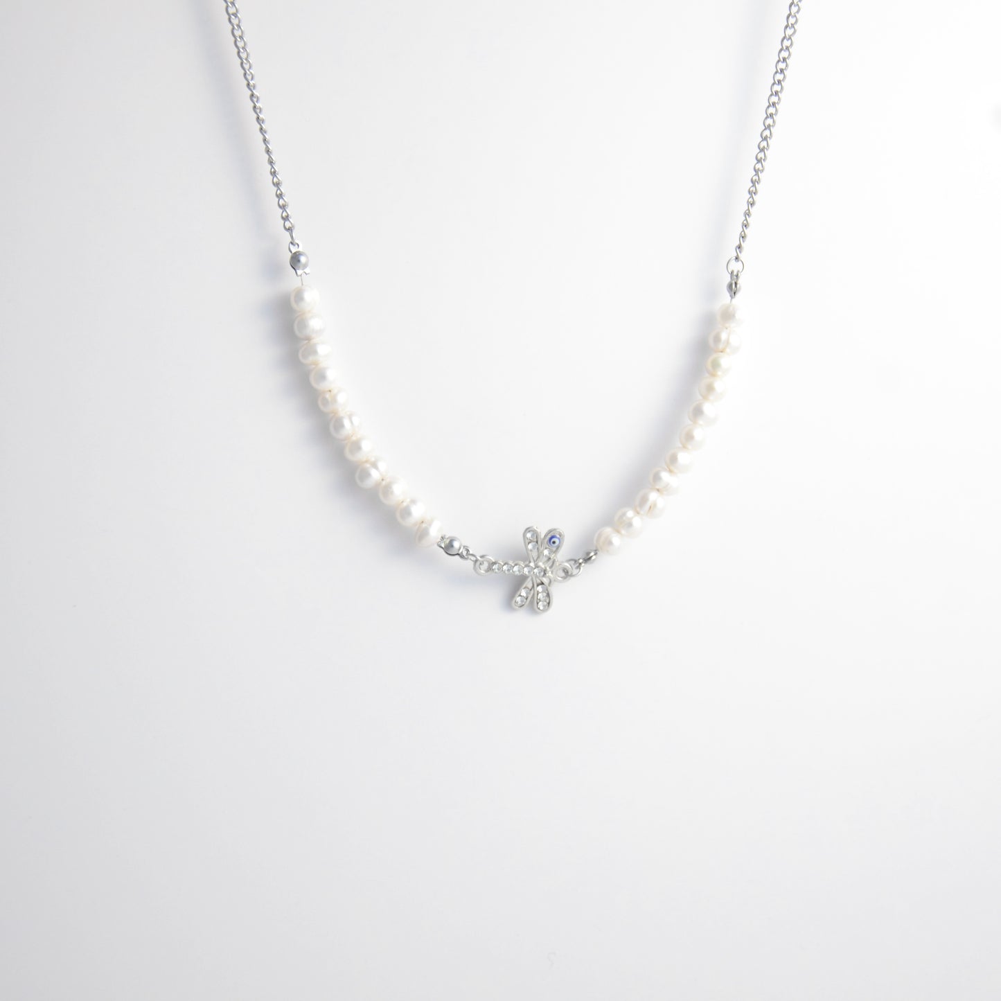 Silver stainless steel pearl choker necklace with a silver dragonfly evil eye pendant on a light gray background