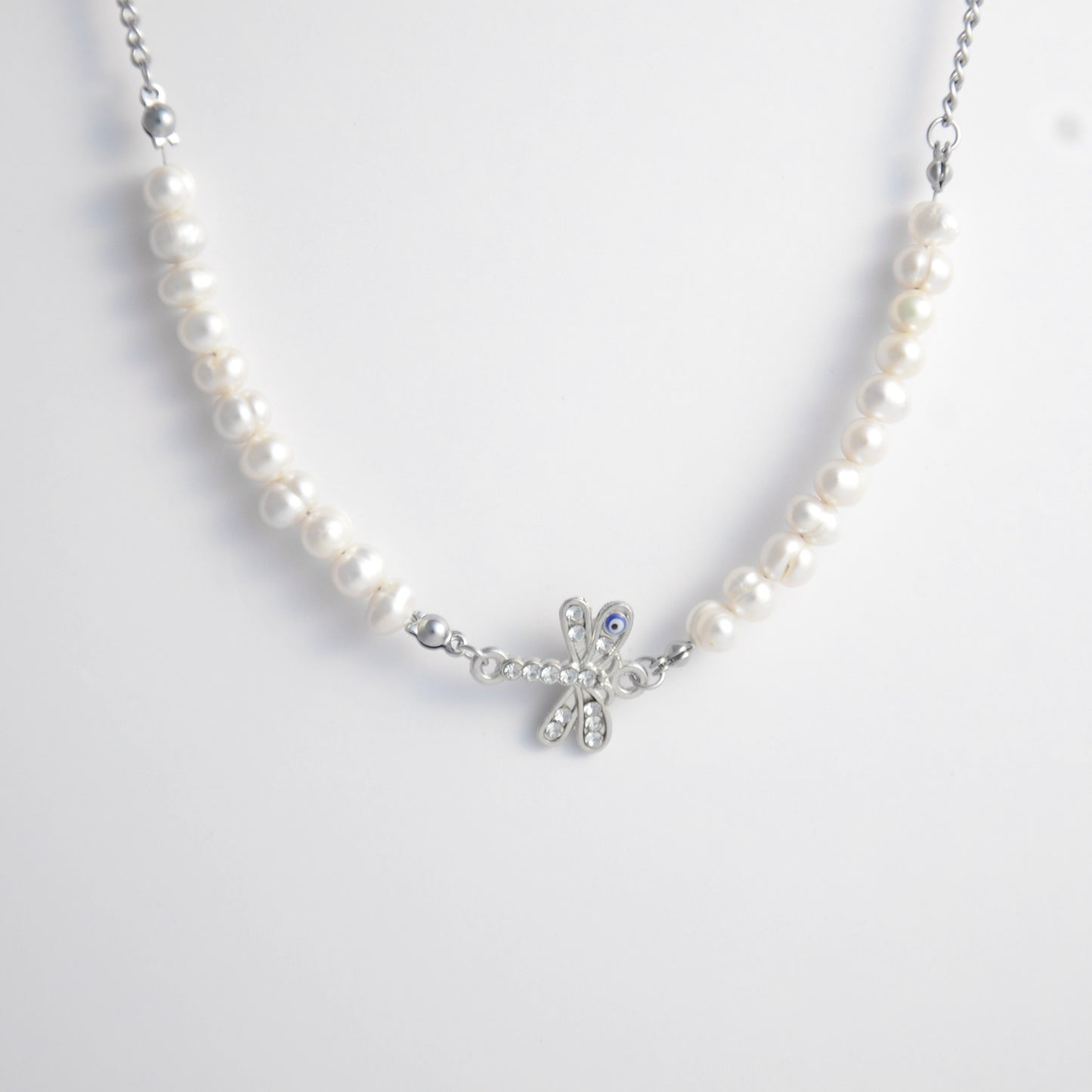 Silver stainless steel pearl choker necklace with a silver dragonfly evil eye pendant on a light gray background