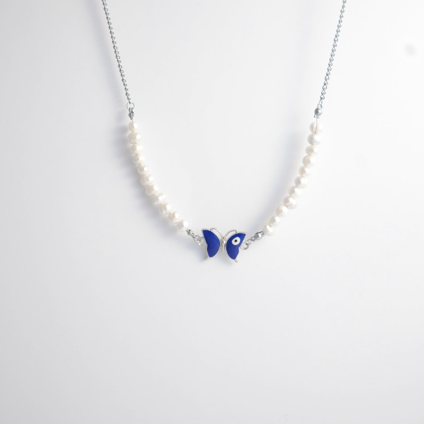 Silver stainless steel pearl choker necklace with a blue butterfly evil eye pendant on a light gray background