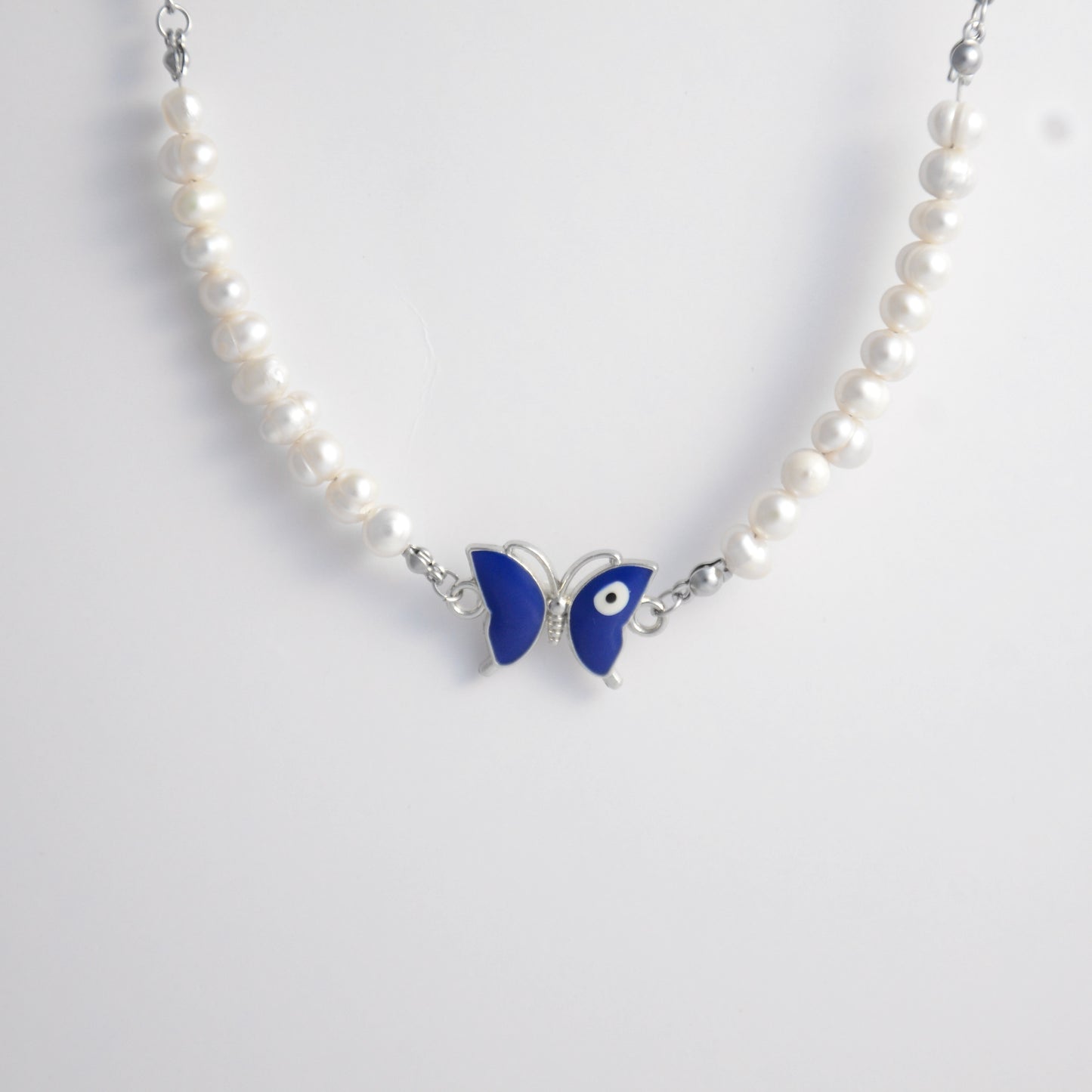 Silver stainless steel pearl choker necklace with a blue butterfly evil eye pendant on a light gray background