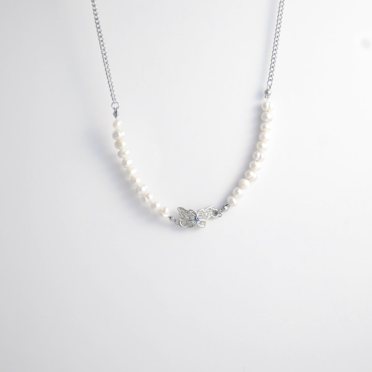 Silver stainless steel pearl choker necklace with a silver butterfly evil eye pendant on a light gray background