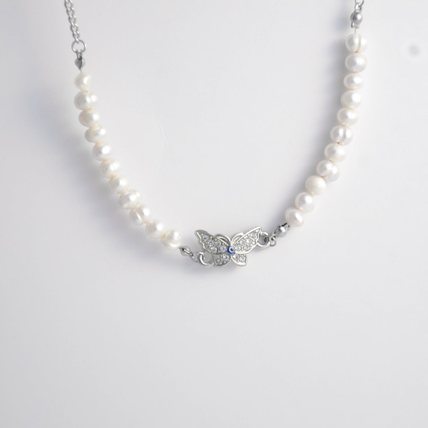 Silver stainless steel pearl choker necklace with a silver butterfly evil eye pendant on a light gray background