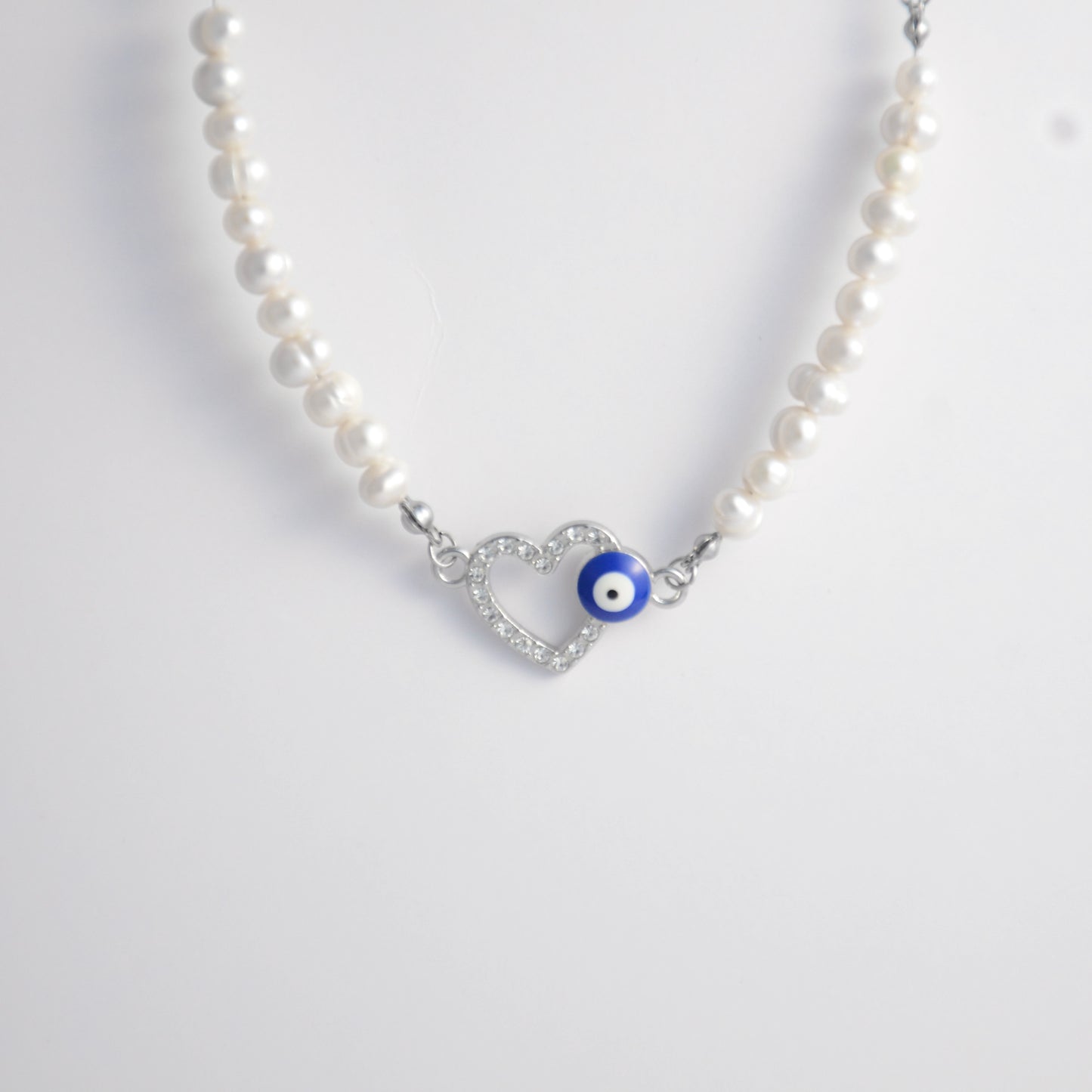 Silver stainless steel pearl choker necklace with a silver heart evil eye pendant on a light gray background