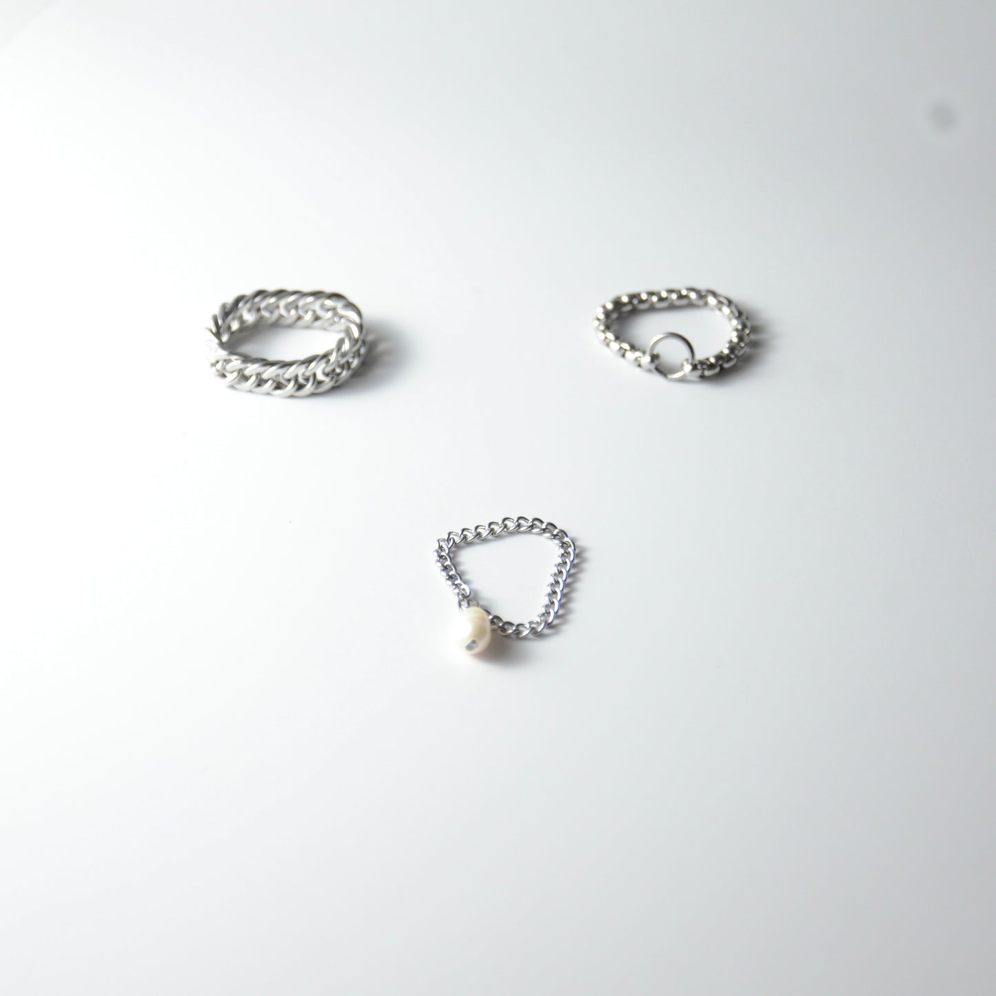 Three silver stainless steel chain rings with pearl charm on a white background