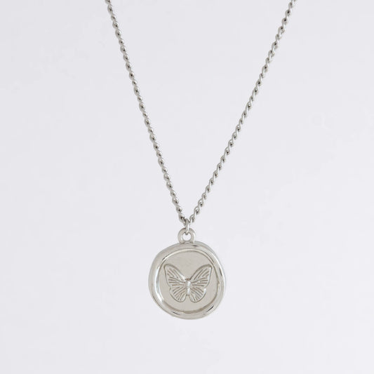 Silver curb necklace with a round butterfly pendant on a light gray background