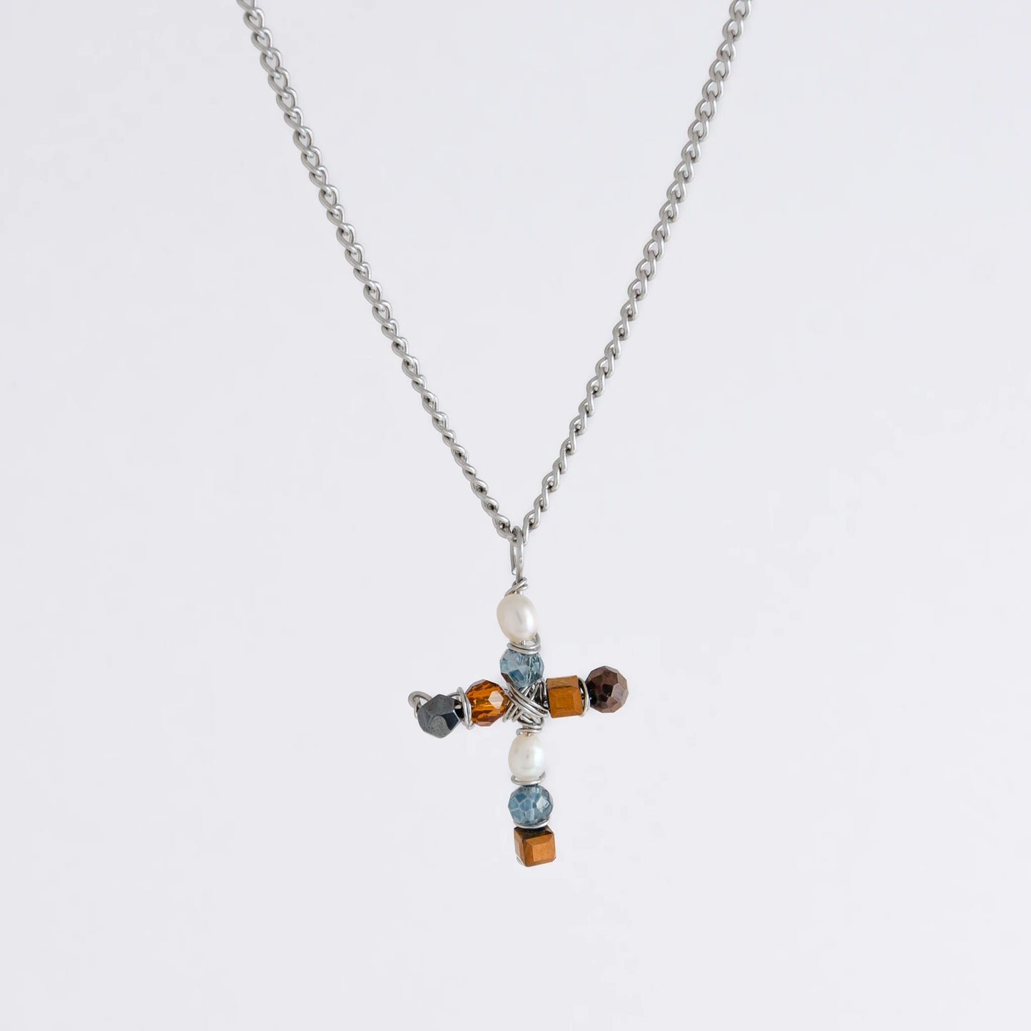 Silver curb chain necklace with a cross pendant made of freshwater pearls and blue, orange and black glass beads on a light gray background