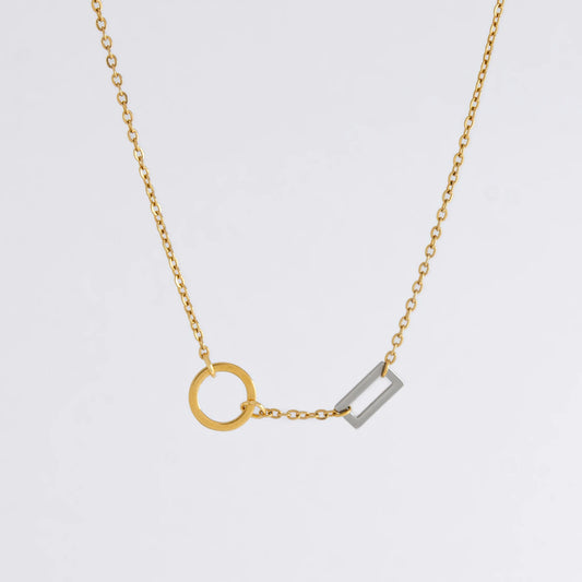 A gold chain necklace with a geometric design featuring a circle of brushed gold and a polished silver bar charm.