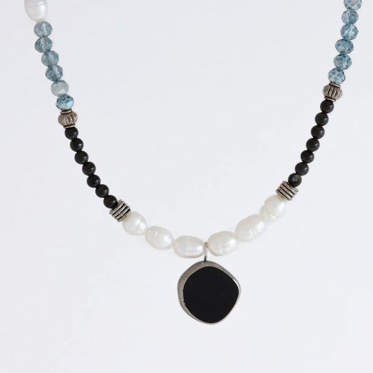 Silver beaded necklace with black pendant and multicolored beads on a light gray background