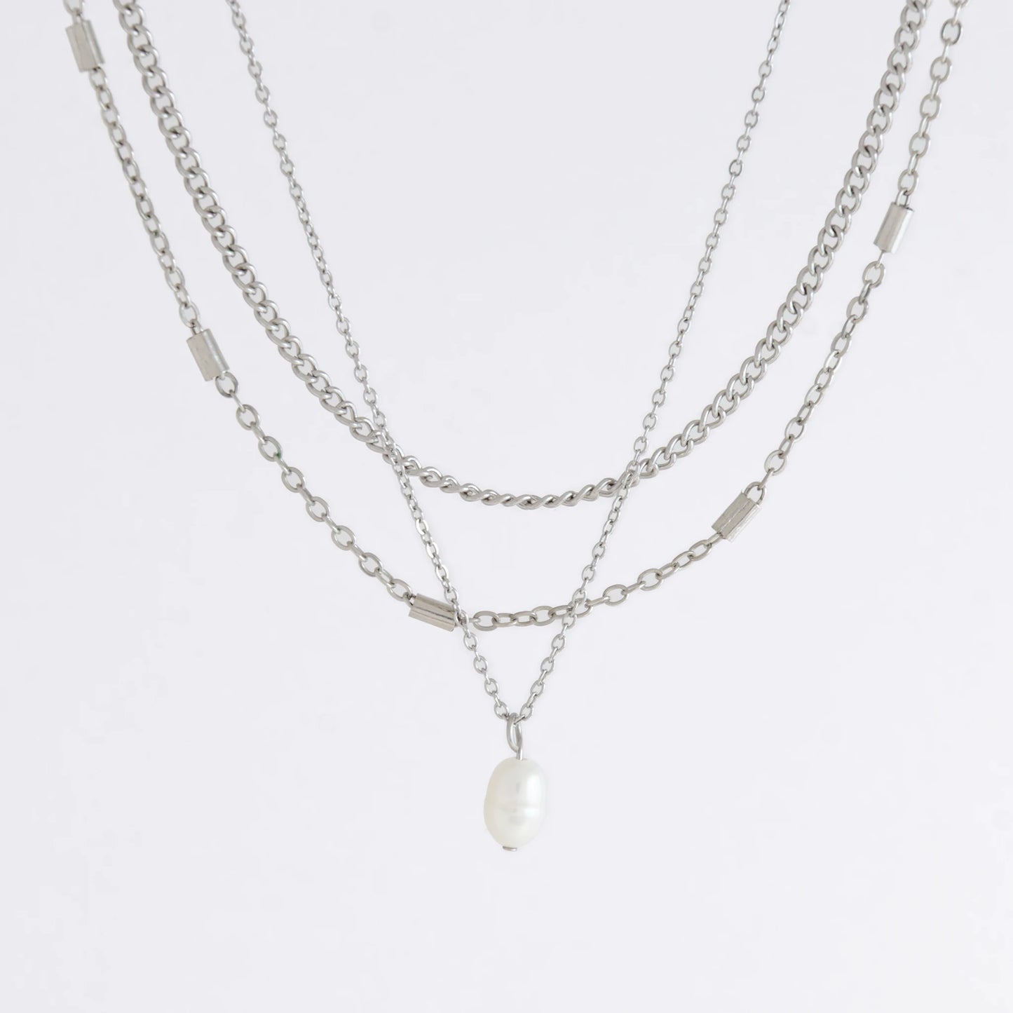 Silver stainless steel layered necklace set with a curb chain, a bar link chain and a dainty pearl pendant necklace on a light gray background
