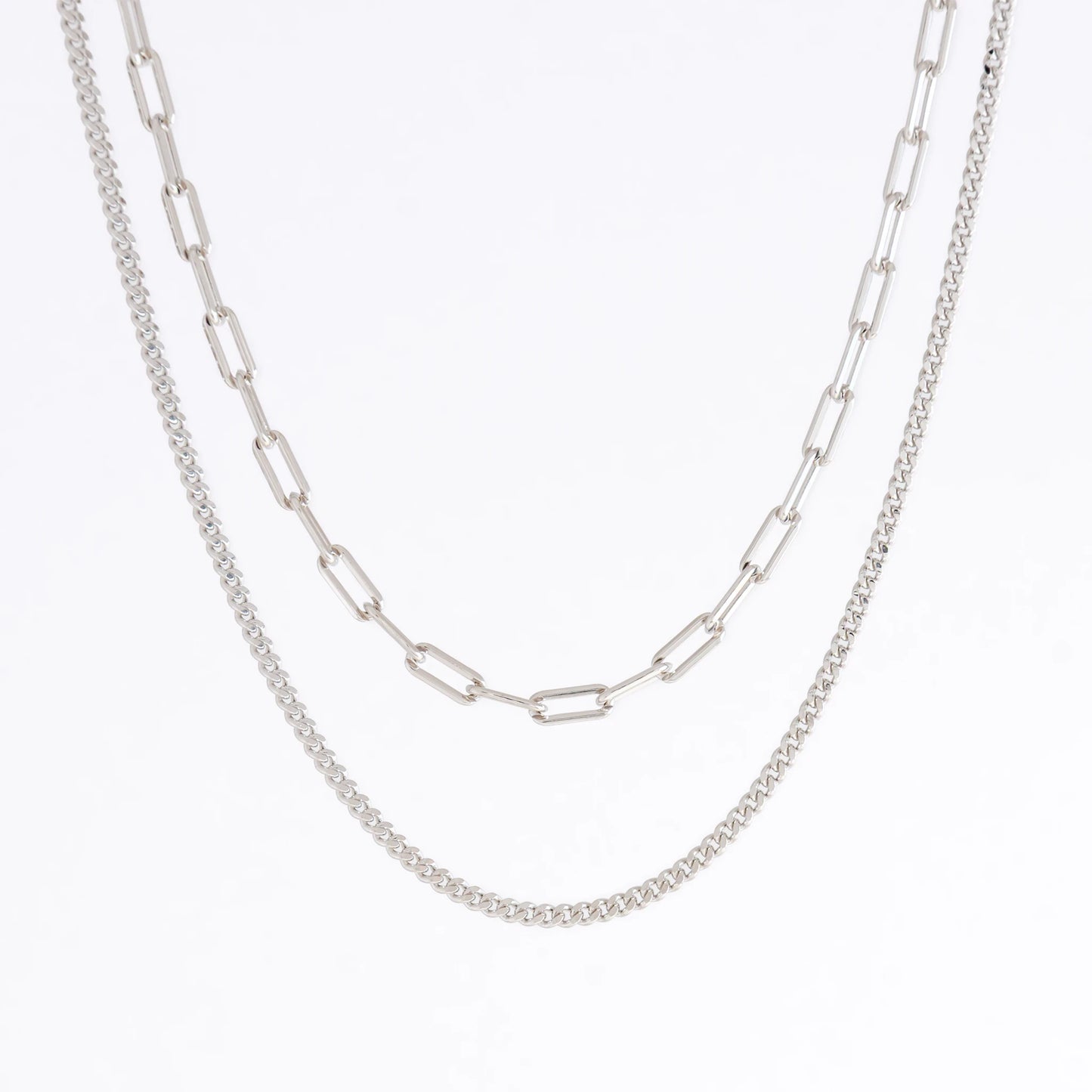 Silver curb chain necklace layered with paperclip necklace on a light gray background