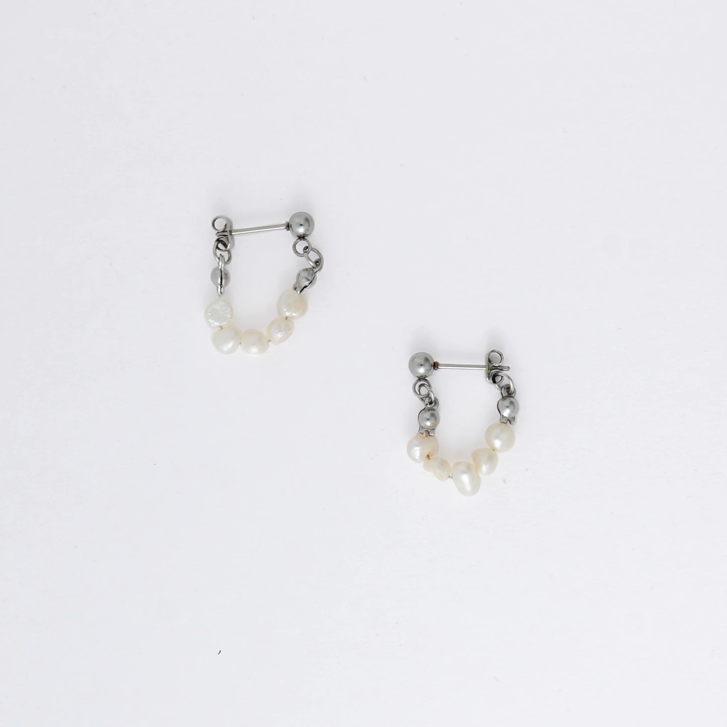 A pair of silver-colored thin pearl hoop earrings, displayed against a white background