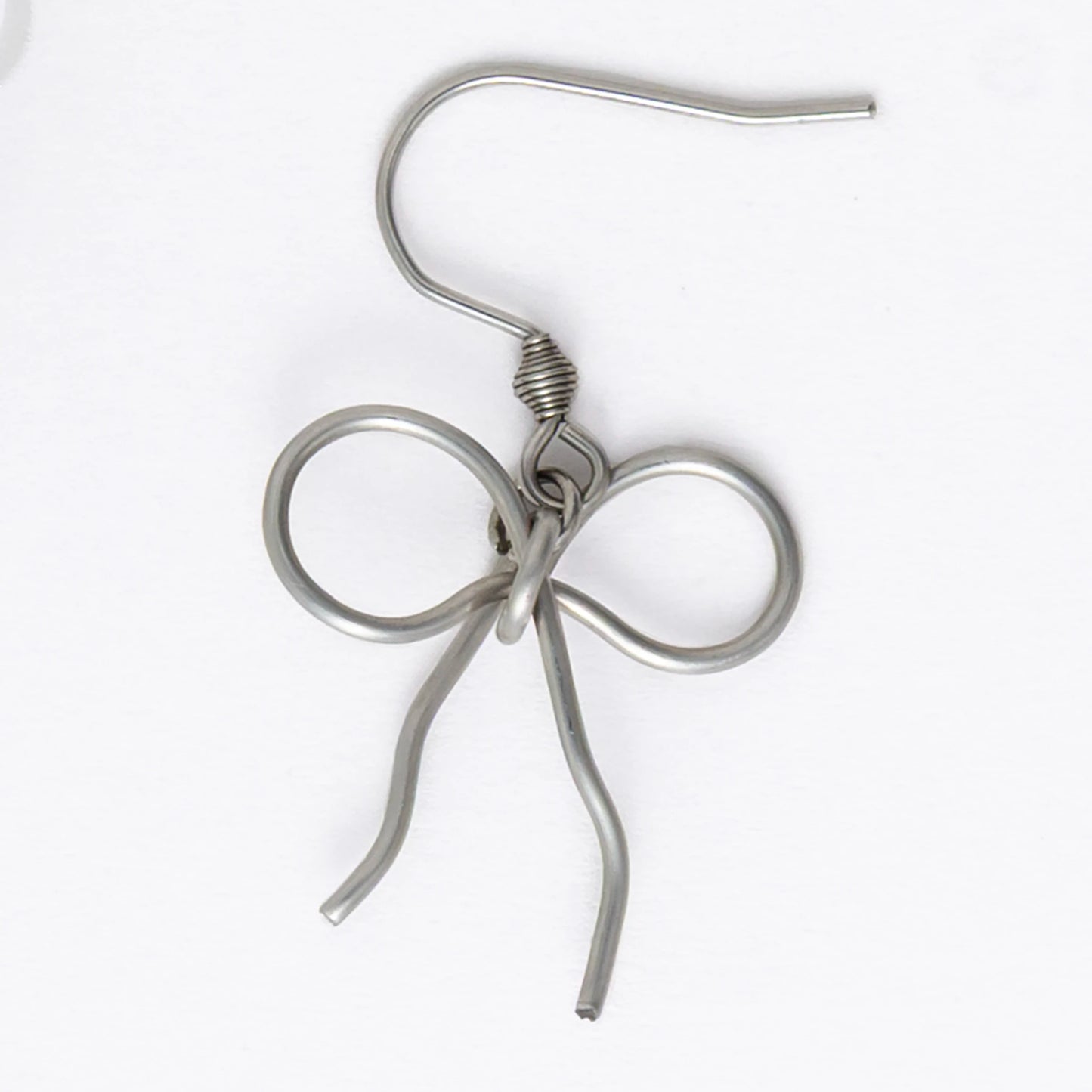 A pair of silver-toned ribbon bow drop earrings on a white background.