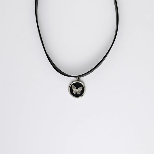 A black leather choker necklace with a central butterfly stamp pendant, displayed against a white background