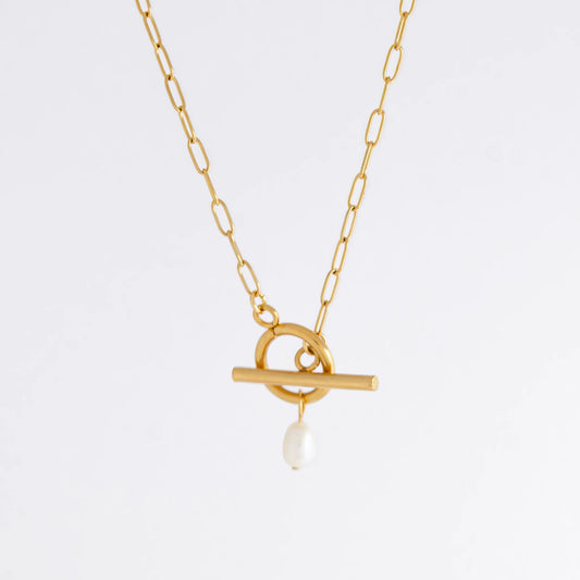 Gold paperclip necklace with toggle clasp and a pearl pendant on a light gray background