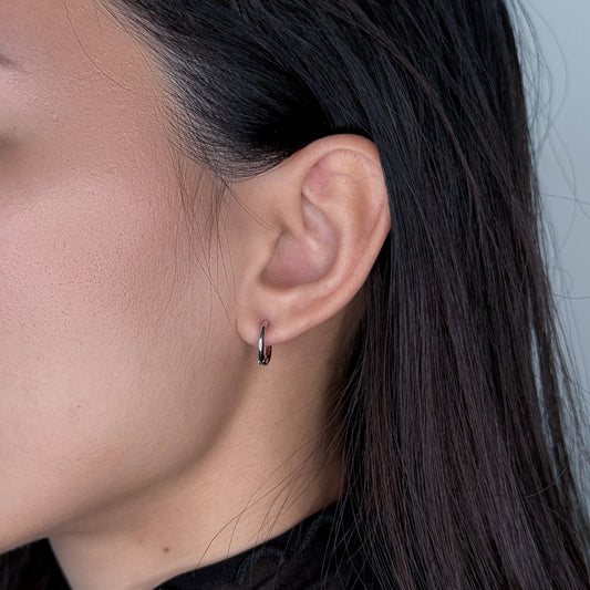Silver huggies hoop earrings worn by model on a gray background