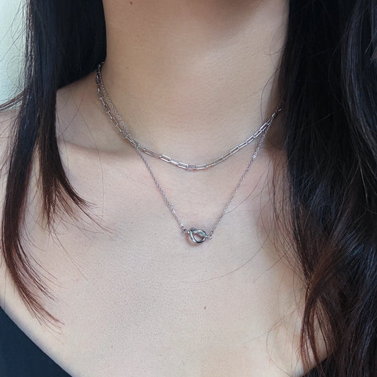 Close-up of a person wearing two silver necklaces with a blurred background