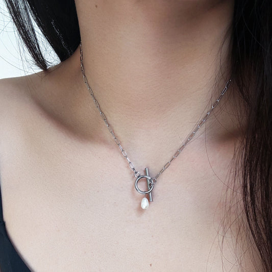 Silver necklace with a pendant featuring a pearl on a person's neck.