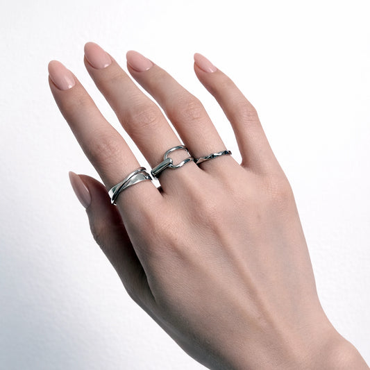 Hand wearing two silver rings on a light gray background